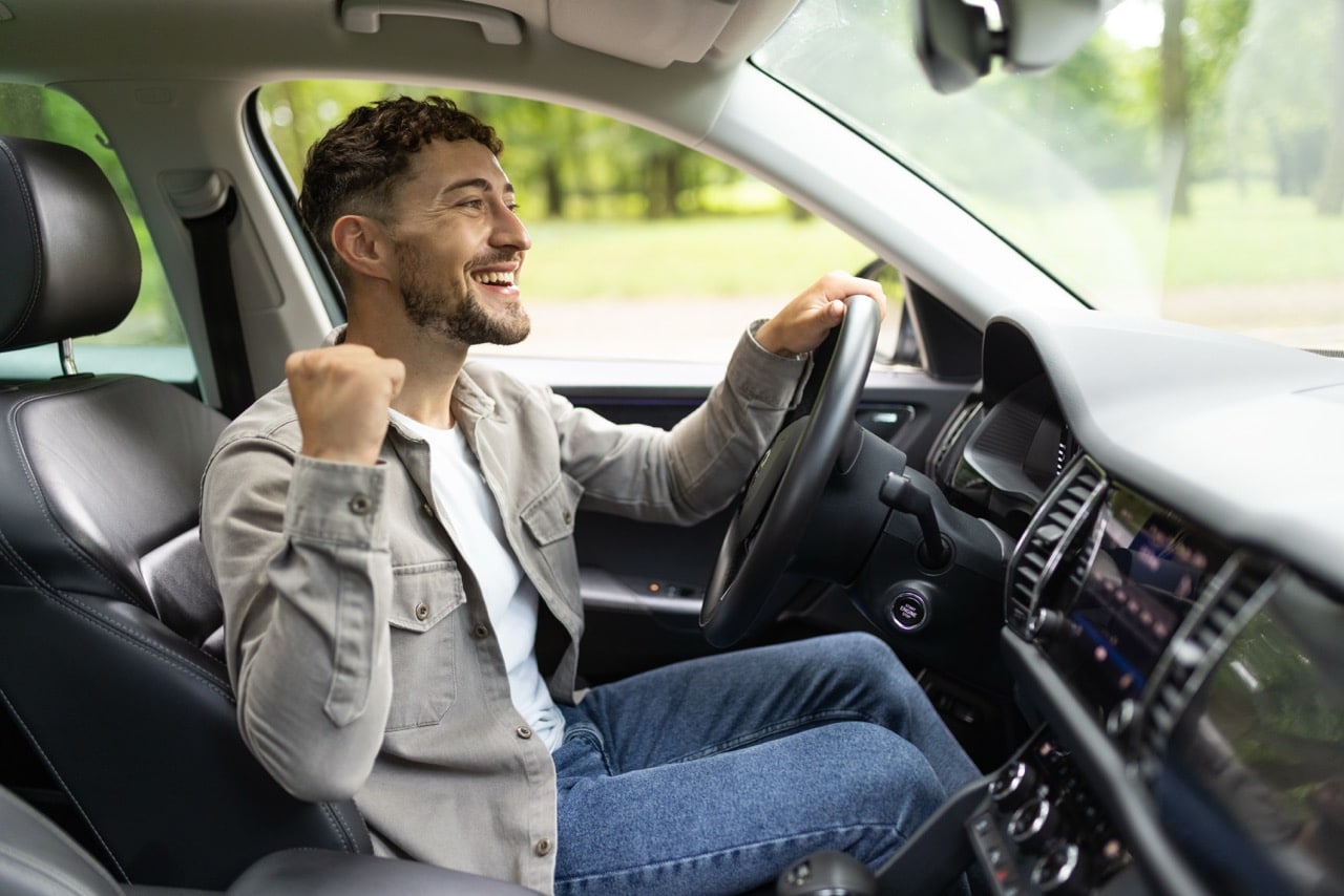 Un homme au volant de sa voiture, content car il a choisi une assurance pour sa voiture qui convient parfaitement à sa situation sans se ruiner