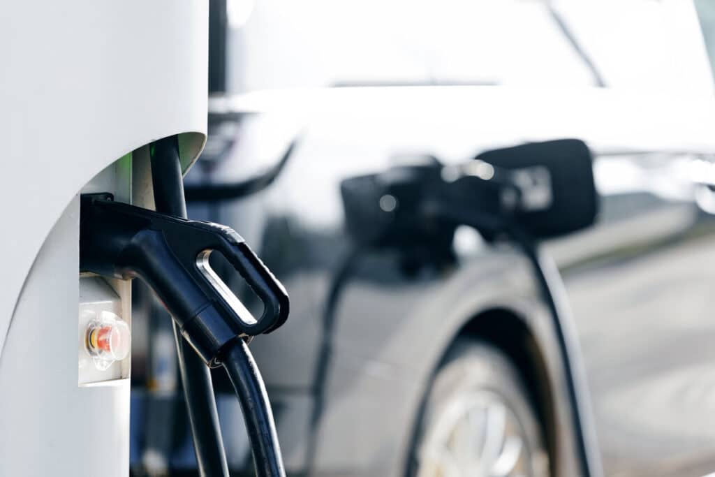 Pistolet de recharge branché sur une borne, une voiture électrique claire garée en arrière-plan